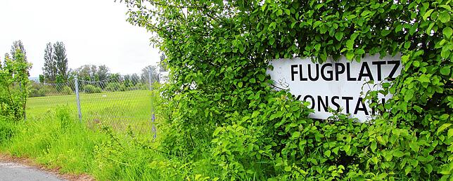 Dezent zugewachsen: Ein Schild, das auf den Flugplatz hinweist.