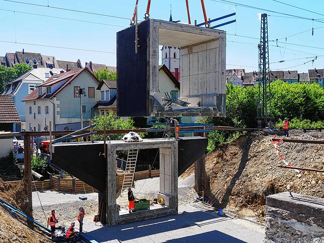 Langsam senkt sich das zweite Fertigteil in Engen dem Boden entgegen. Unten fixieren Arbeiter das teil mit langen Eisenstangen.