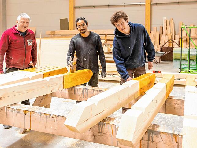Zwei angehende Köche helfen in der Halle des Zimmereibetriebs Kostenbader beim Balkenstreichen (von links): Axel Kostenbader, Panji ...