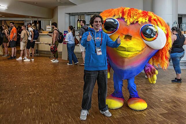 Finn Börner posiert mit Lumo, dem Maskottchen des 69. Eurovision Song Contests, das die freiwilligen Helfer in Basel begrüßt.