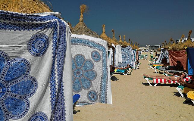 Auf Mallorca schützen Menschen sich mit Strandtüchern vor der Sonne.