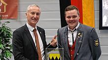 Der Vorsitzenden des Musikvereins Schwenningen, Adrian Deufel, erhält von Bürgermeister Ewald Hoffmann das Gemeindewappen in Glasausführung.