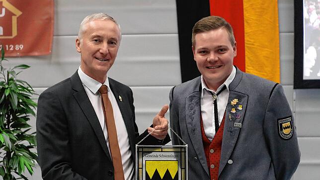 Der Vorsitzenden des Musikvereins Schwenningen, Adrian Deufel, erhält von Bürgermeister Ewald Hoffmann das Gemeindewappen in Glasausführung.