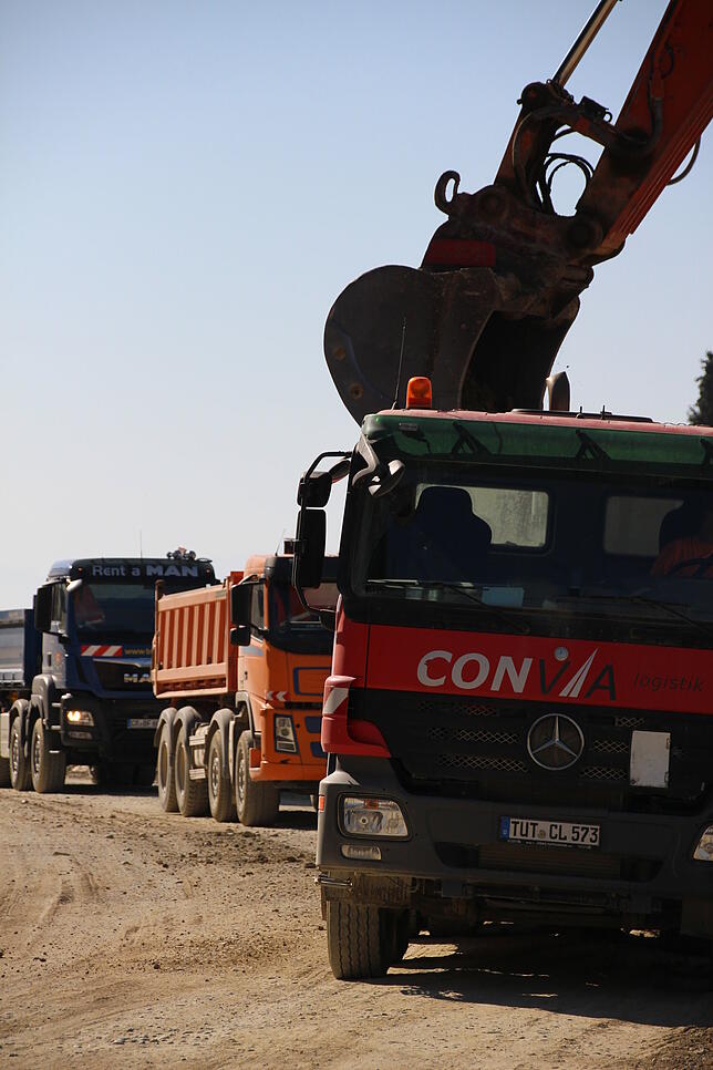 Während ein LKW mit Erdaushub beladen wird, warten im Hintergrund bereits weitere, um eine durchgehende Arbeit zu ermöglichen.