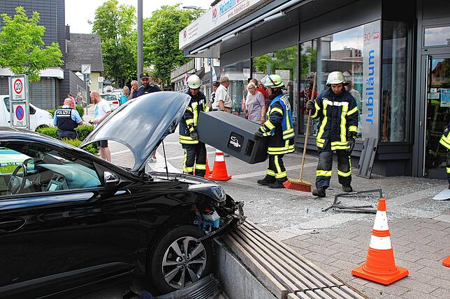 Feuerwehrleute räumen einen Mülleimer beiseite, in den das Auto gefahren war.