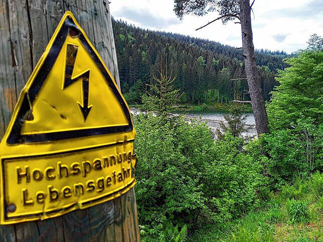 Ein Hinweisschild warnt vor Hochspannung. Im Hintergrund ist die Linachtalsperre bei Vöhrenbach im Südschwarzwald zu sehen. Nicht nur ...