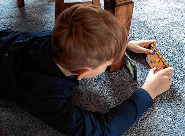 Ein Junge spielt ein Videospiel auf seinem Smartphone und überträgt es mit einem zweiten Handy per Facetime zu seinem Freund.