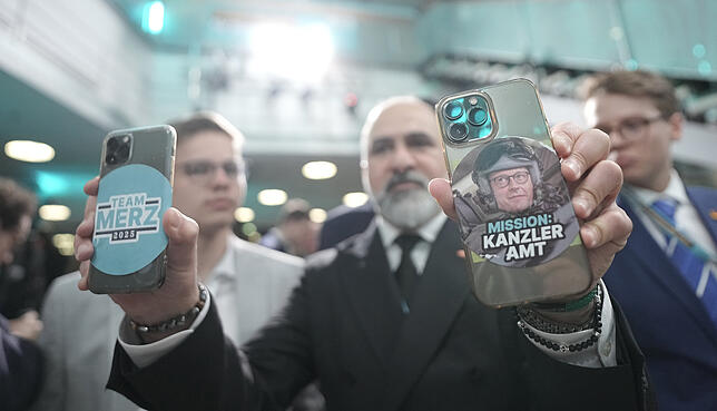 Ein CDU-Anhänger hält im Konrad-Adenauer-Haus Smartphone mit Merz-Aufklebern hoch.
