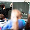Eine Lehrerin schreibt in einer Grundschule an eine Tafel. Lehrer sowie Erzieherinnen an Kitas dürfen sich seit diesem Montag gegen das ...