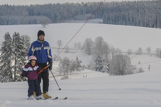 Ein Vater lässt sich mit seinem Kind an einem Schlepplift den Berg hinauf ziehen.