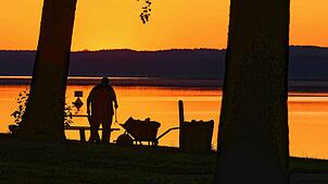 Ein Mann reinigt am frühen Morgen des 2.7.2025 eine Liegewiese am Scharmützelsee. Der Deutsche Wetterdienst warnt teils vor extremer Hitze.