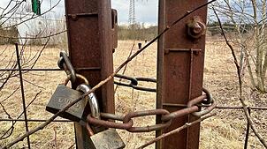 Schlösser am Tor und ein Zaun sichern das Gelände, auf dem die 2019 abgeschaltete Grundwasserreinigungsanlage (weißes Gebäude) steht. ...