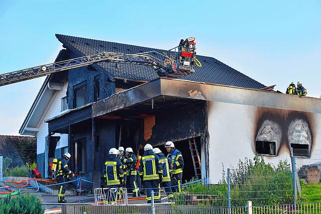 Feuerwehrleute stehen vor der ausgebrannten Garage.