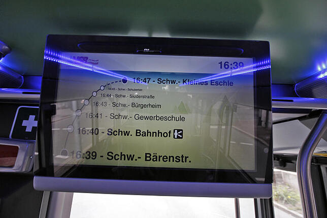 Eine Anzeige informiert Fahrgäste, wo sich der Bus aktuell befindet. Blaue Lichtleisten an der Decke sorgen für angenehmes Ambiente.