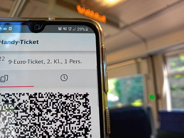 Ein Fahrgast hält sein Handy mit dem Neun-Euro-Ticket in der Hand.