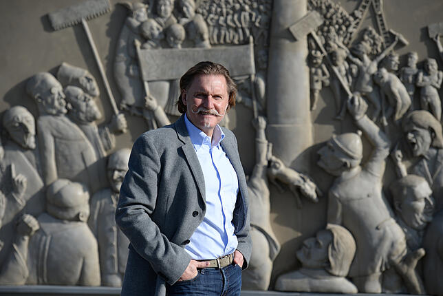 TV-Anwalt Ingo Lenßen posiert in Bodman-Ludwigshafen vor einem Wandrelief des Künstlers Peter Lenk.
