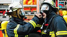 (Symbolbild) Zwei Feuerwehrmänner schließen sich während einer Übung vor einem Löschfahrzeug die Atemschutzgeräte an.