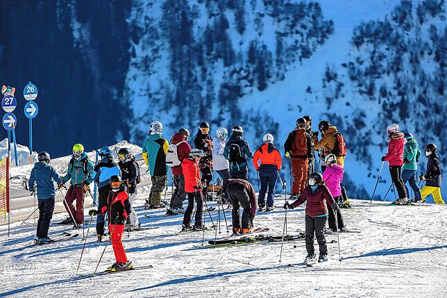 In St. Anton am Arlberg stehen Skifahrer an einer Piste. Man muss voll durchgeimpft sein, um Ski zu fahren.