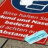 Eine getragene Mund-Nase-Bedeckungsmaske liegt auf einem Aufkleber, der auf die Maskenpflicht hinweist.