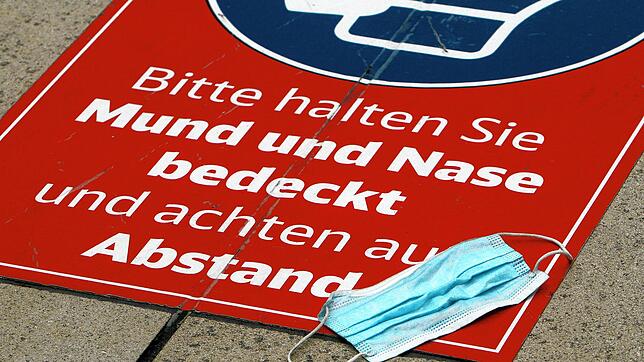 Eine getragene Mund-Nase-Bedeckungsmaske liegt auf einem Aufkleber, der auf die Maskenpflicht hinweist.