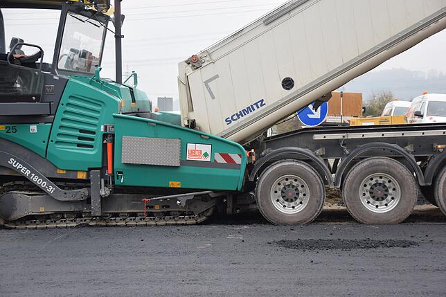 Ein Lastwagen beliefert den Beschicker mit Asphalt.