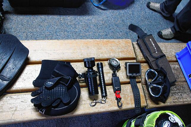 Zur Ausstattung zählen unter anderem Handschuhe, zwei Lampen, ein Kompass, ein Tauchcomputer, eine Schwimmbrille und ein Bleigurt.