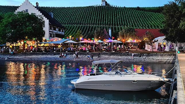 Blick vom Bootsanleger auf das Rebgut Haltnau. Der zugehörige Biergarten ist im Vordergrund zu erkennen, bunte Lichterketten sorgen für ...
