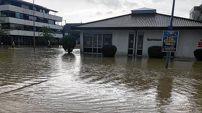 Zwei Einsatzkräfte kämpfen sich nach dem Unwetter am 26. Juni durch das Wasser, dass ihnen bei der Sparkasse bis zu den Knien steht.