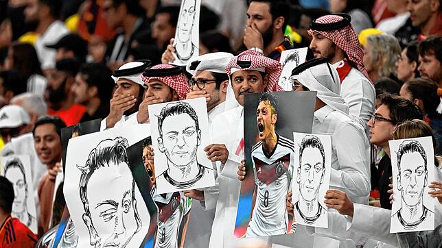 Zuschauer halten im Al-Bait Stadion in Katar Bilder von Deutschlands ehemaligem Nationalspieler Mesut Özil in die Höhe und halten sich ...