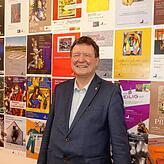 Dr. Edwin Ernst Weber vor der Plakatwand, die die von ihm intiierten und begleiteten Ausstellungen zeigt.