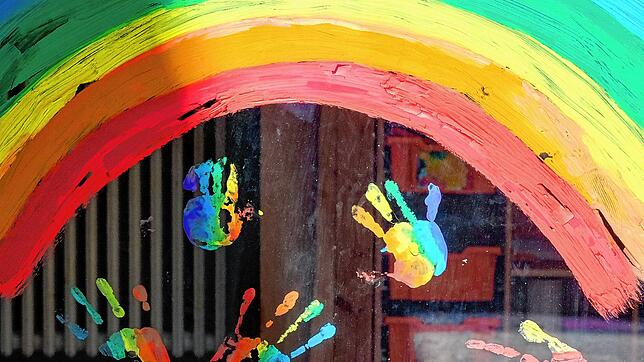 Kinderhände und ein Regenbogen sind an einer Kita zu sehen.