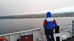 Nur wenige Menschen zieht es auf der Fähre von Konstanz nach Meersburg an die Reling, das Bodensee-Panorama ist von Nebelwolken umhüllt.