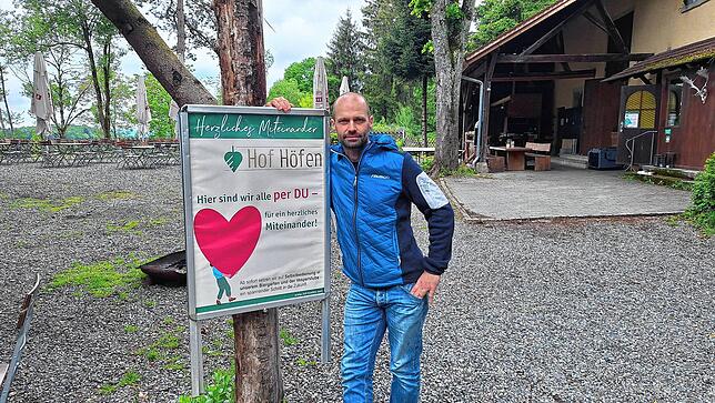 Alex Rommel vor einem Hinweisschild in Hof Höfen. Im Hintergrund der Biergarten, der ab 15. Mai von Freitagabend bis Sonntag sowie an ...