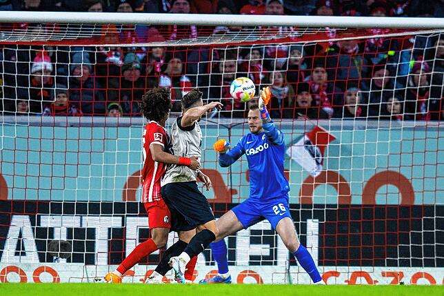Freiburgs Torwart Mark Flekken (r) hält einen Ball kurz vor Ende des Spiels von Augsburgs Ermedin Demirovic (M).