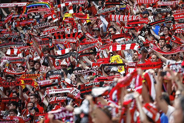 Fans des SC Freiburg halten ihre Schals hoch.