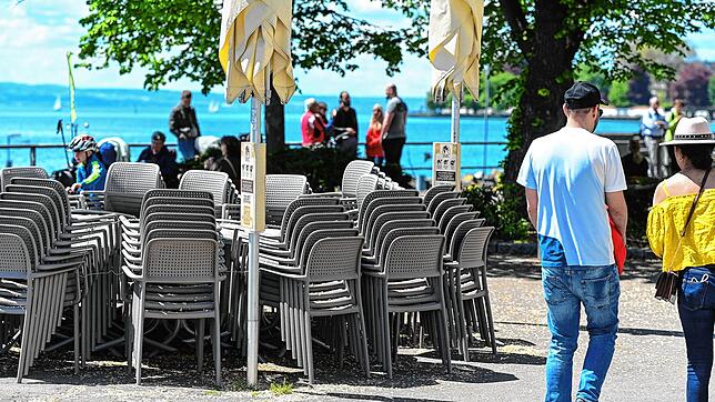 Blick nach Friedrichshafen am Wochenende: Stühle und Tische stehen aufgereiht an der Uferpromenade, während im Hintergrund Passanten ...