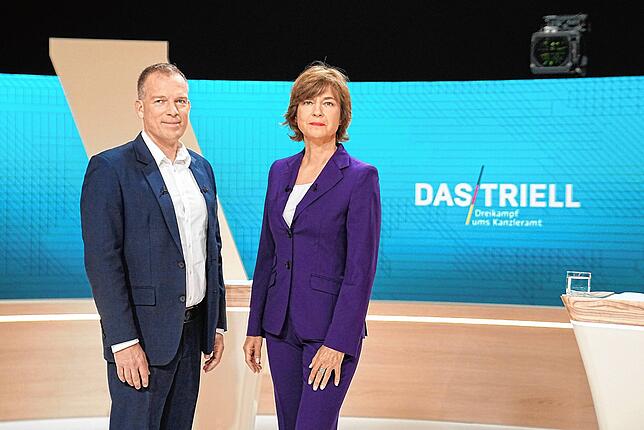 Die Moderatoren Oliver Köhr und Maybrit Illner stehen im Fernsehstudio und fühlen den Kanzlerkandidaten auf den Zahn.