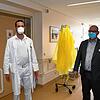 Mit Mundschutz zur Sicherheit, im Hintergrund hängen die gelben Schutzkittel für die Arbeit mit Patienten, die positiv auf das ...