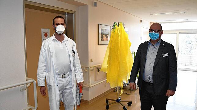 Mit Mundschutz zur Sicherheit, im Hintergrund hängen die gelben Schutzkittel für die Arbeit mit Patienten, die positiv auf das ...