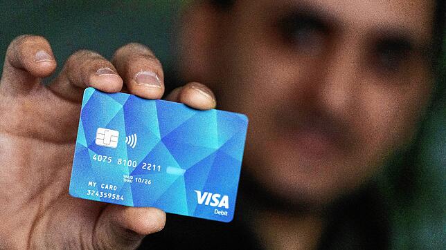 Ein Geflüchteter hält eine Debitcard in der Hand (Symbolbild). Ab Januar sollen Asylbewerber in mehreren Pilotlandkreisen im Land mit ...