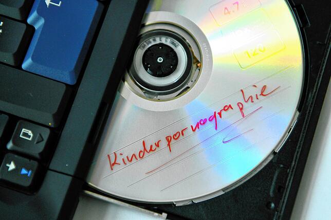 Eine DVD mit der Aufschrift “Kinderpornographie„ liegt im Laufwerk eines Notebooks.