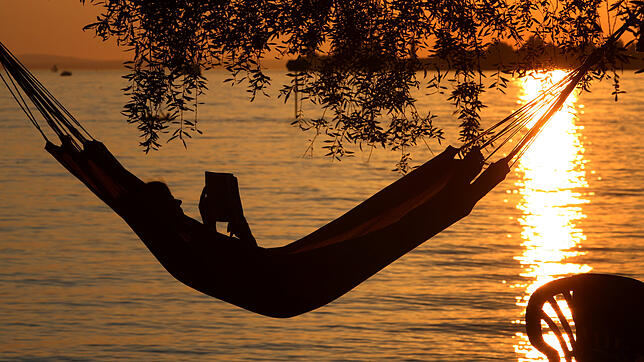 Eine Frau liest in einer Hängematte am Badestrand eines Campingplatzes in Lindau ein Buch. Viele Beschäftigte träumen davon, einmal für ...