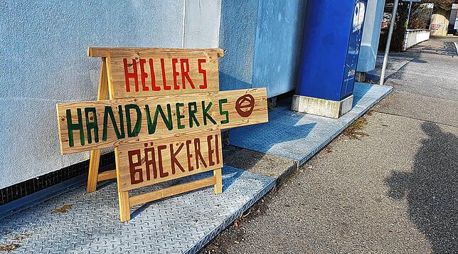 Mit einem Holzschild an der Wilhelm-Binder-Straße wirbt Bäckermeister Adolf Heller für seine kleine Handwerksbäckerei.