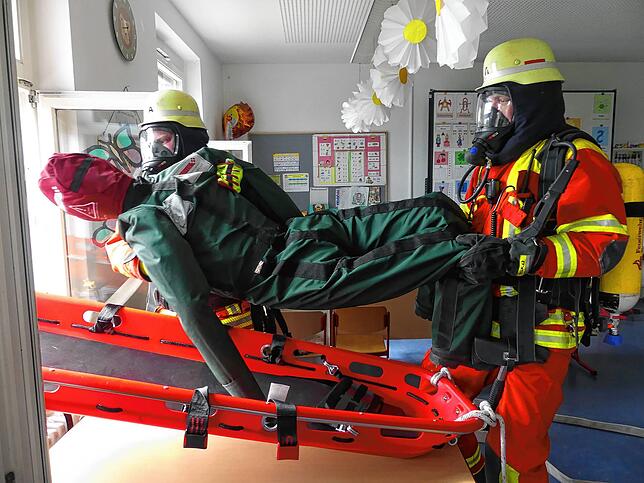 Die vermeintlich ohnmächtige Person, hier ein Dummy, wird von zwei Feuerwehrmännern auf die Trage gelegt und vom oberen Stockwerk nach ...