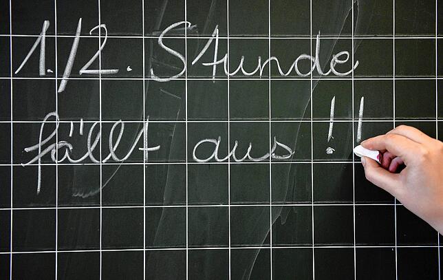 Eine Lehrerin schreibt in einer Grundschule den Satz „1./2. Stunde fällt aus!!“ an die Tafel. Die GEW in Südbaden ärgert ...