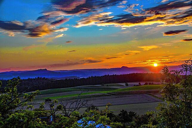 Im Blick von Duchtlingen auf den Hegaulandschaft geht die Sonne vor Hohenstoffel und Hohenhewen am Horizont unter.