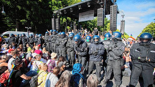 Polizisten stehen Anfang August bei einer Kundgebung gegen die Corona-Beschränkungen in Berlin zwischen Teilnehmern vor einer Bühne. Zu ...