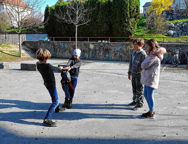 Symbolfoto: Einem Jungen wird die Jacke gewaltsam weggerissen und die Mitschüler schauen belustigt zu.
