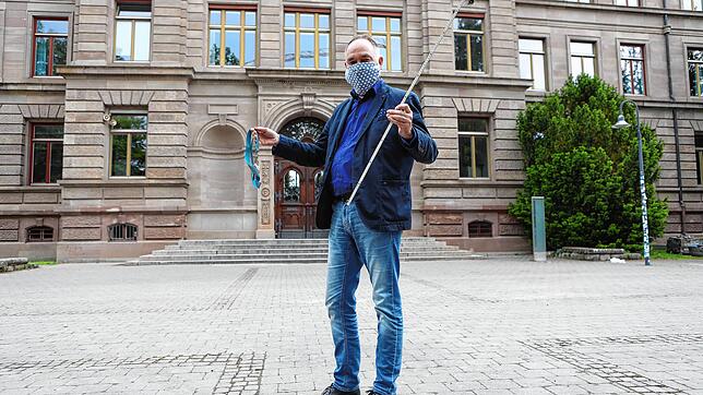 Jürgen Kaz steht vorschriftsmäßig mit Mundschutz und einem Zollstock zum Ausmessen des Mindestabstands vor dem Humboldt-Gymnasium.