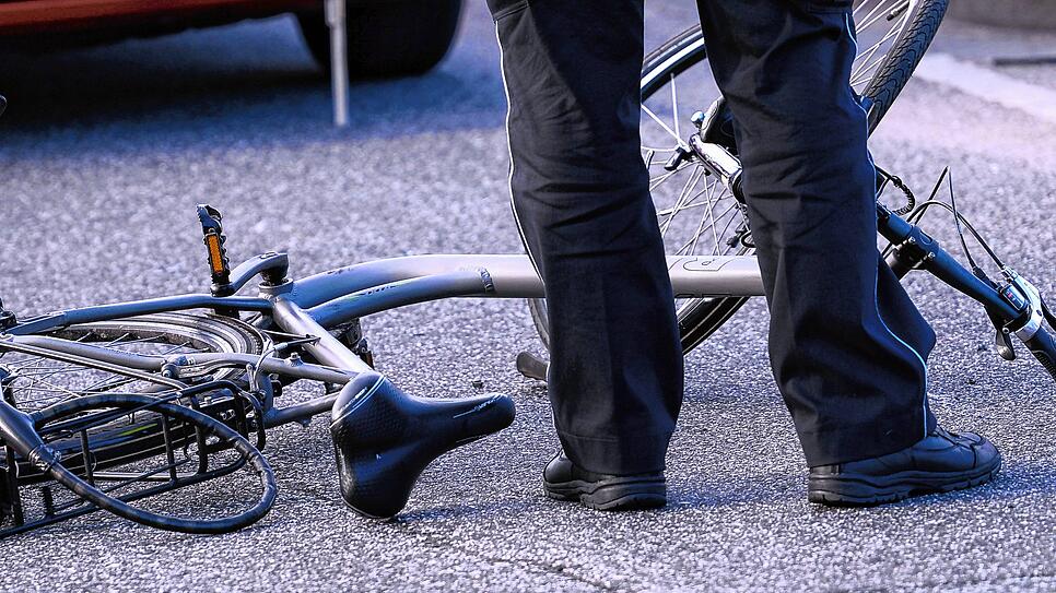 Unser Symbolbild zeigt einen Beamten, der einen Fahrradunfall aufnimmt. Ein beschädigtes Fahrrad liegt vor einem Auto auf der Straße.